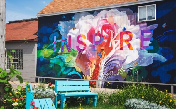 Part of a garden looking towards a house, on which is painted a colourful mural of a flower and the word 'inspire'